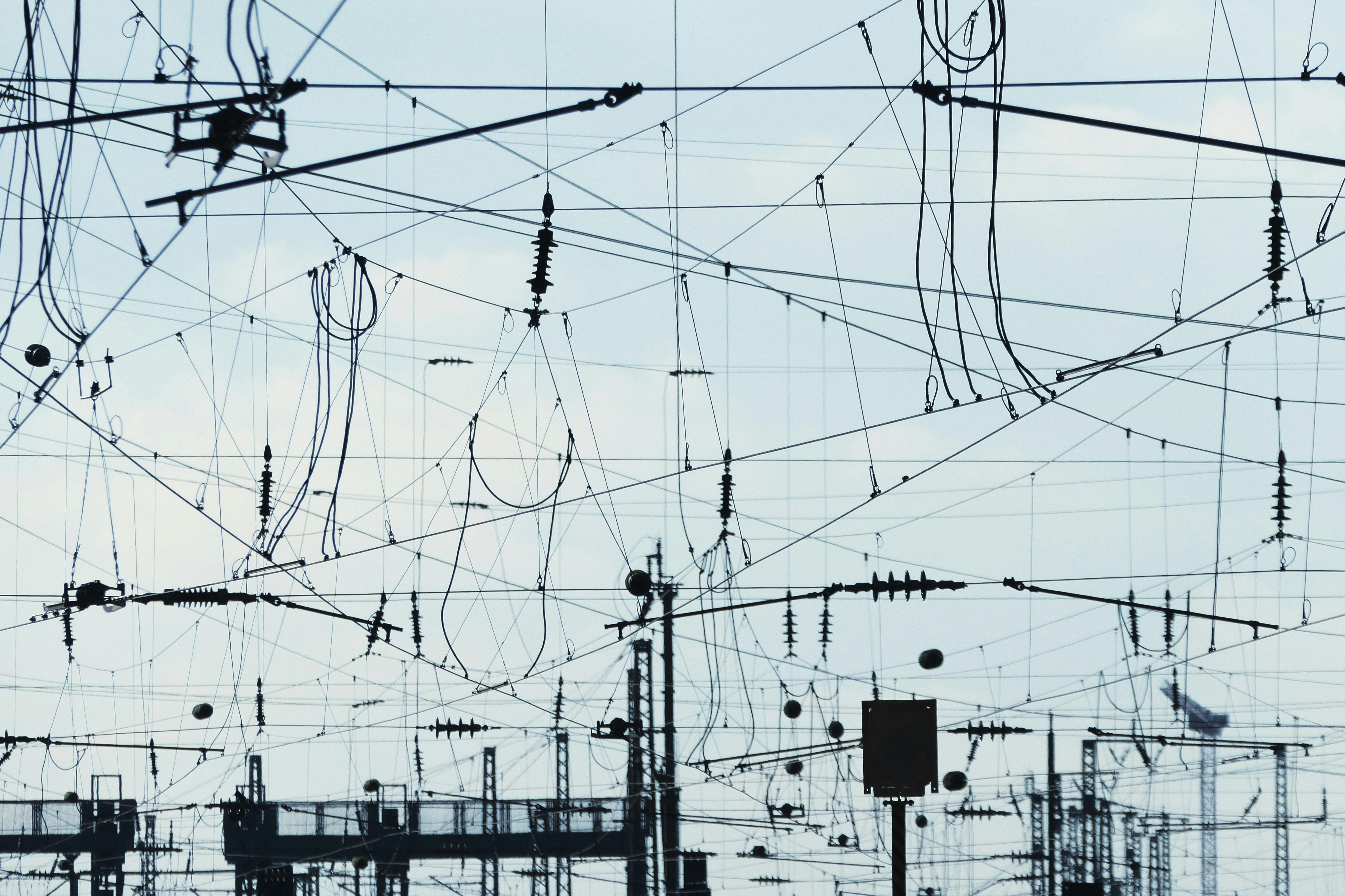 A tangled web of overhead power lines and cables against a pale sky
